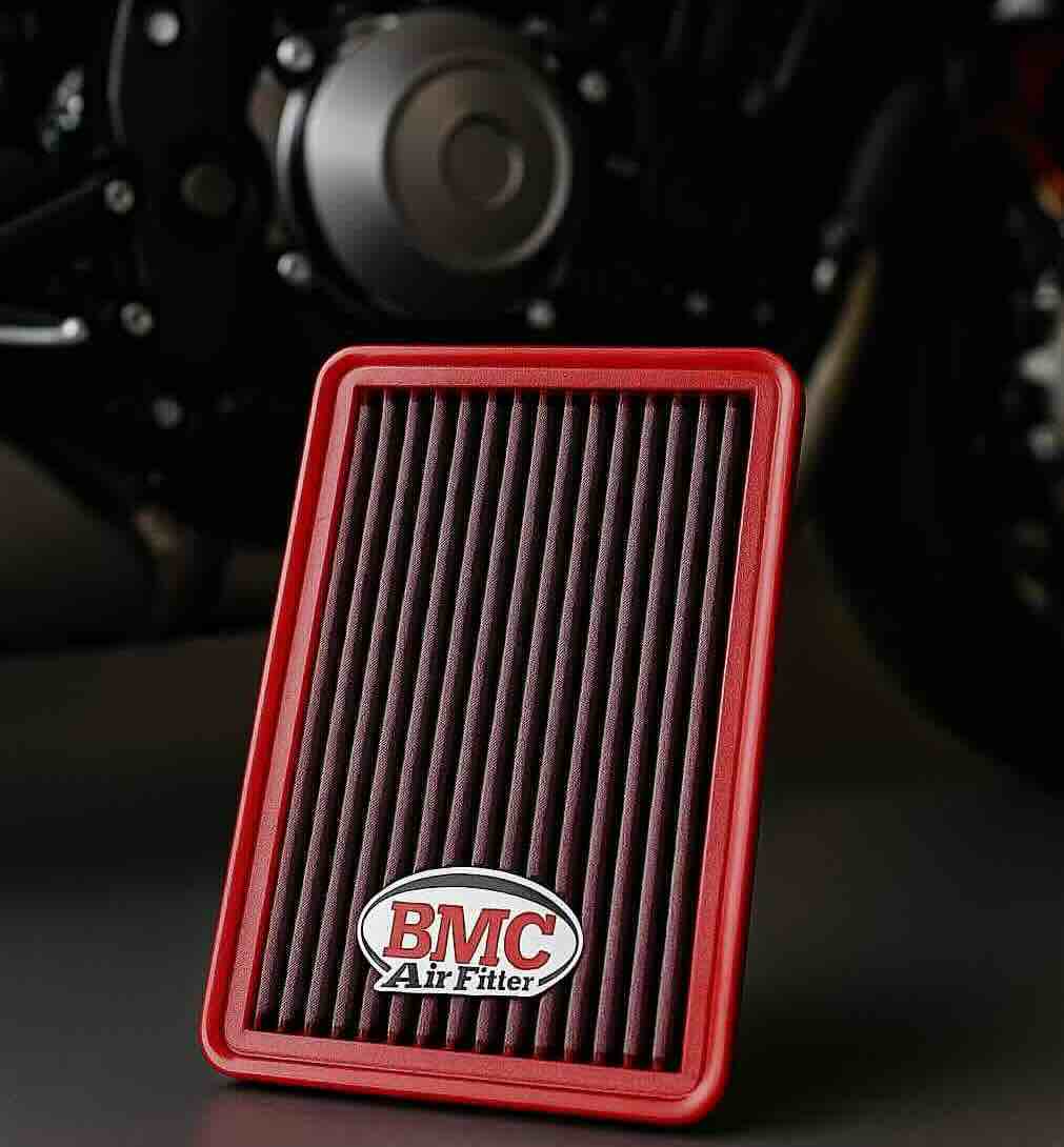 Red BMC motorcycle air filter in front of a sport bike engine, showcasing washable and reusable design for Ducati, Yamaha, Honda, and BMW motorcycles.
